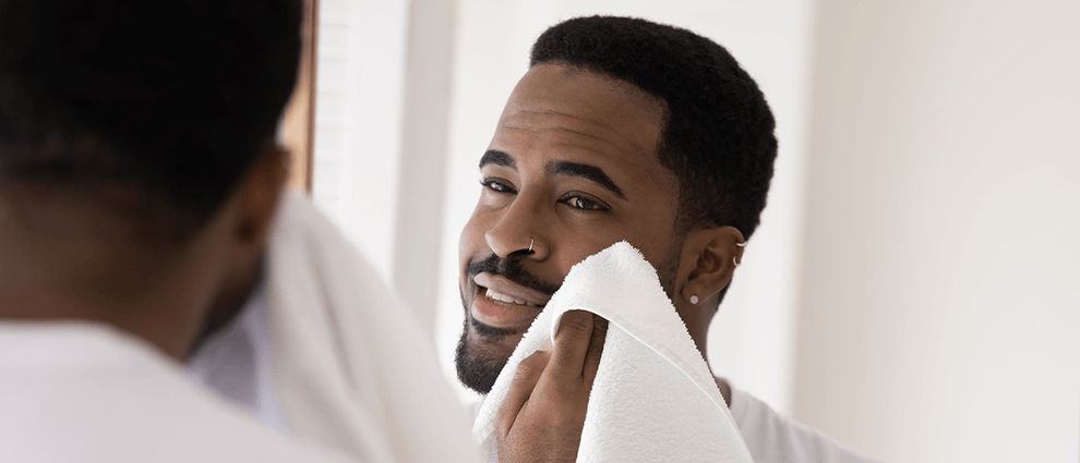 Como aparar a barba: homem negro adulto, usando corte flat top no cabelo, passando uma toalha branca sobre a barba.
