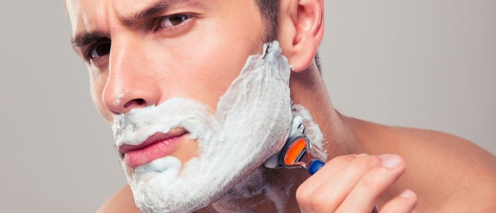 Homem fazendo a barba com espuma de barbear em seu rosto.