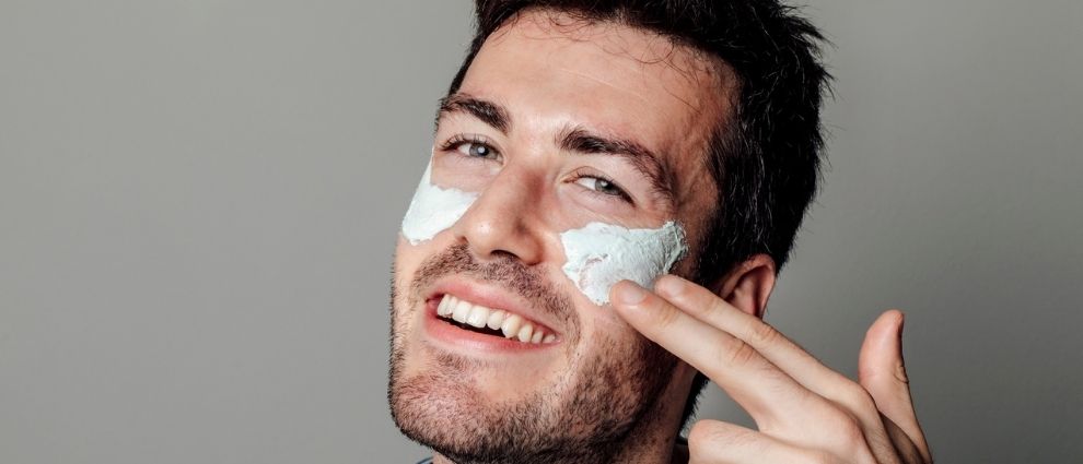 Homem aplicando uma máscara de skincare em seu rosto.