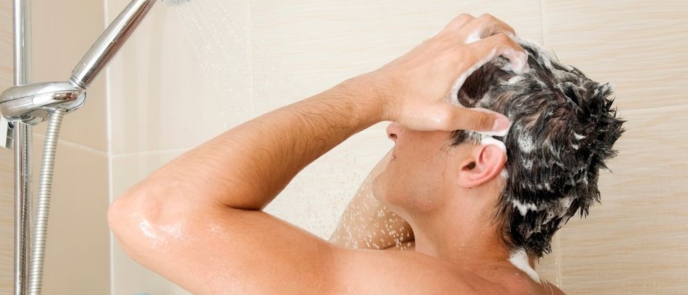 Homem tomando banho e esfoliando o couro cabeludo.