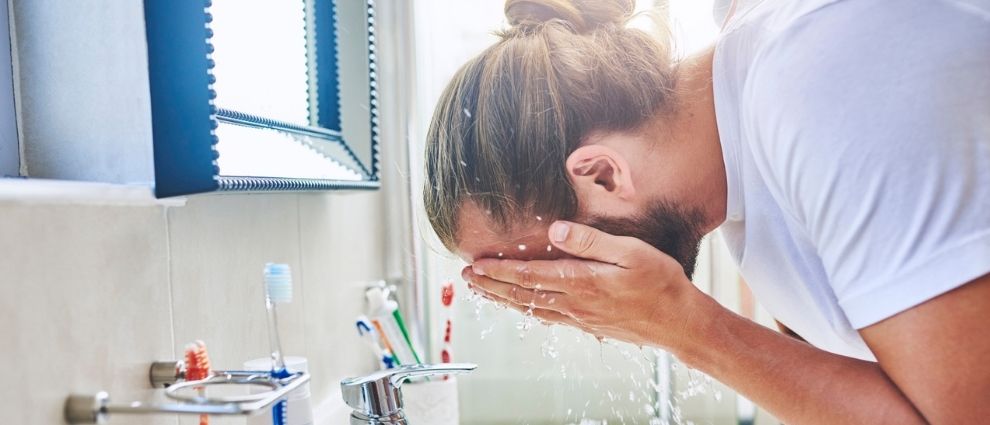 Homem de cabelo longo lavando o rosto.