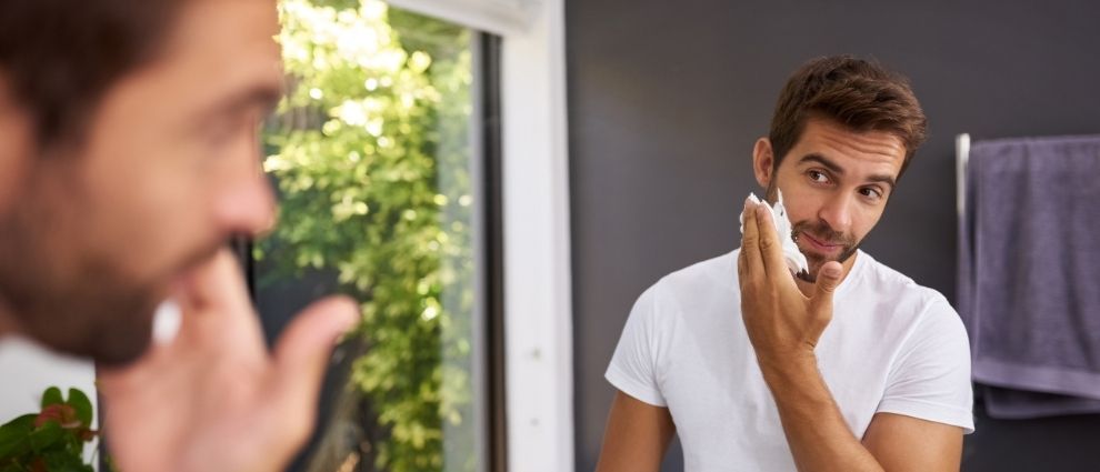 Homem aplicando shampoo para barba em seu rosto.