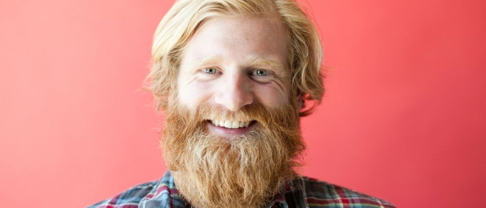 Homem de barba e cabelo longos sorrindo.